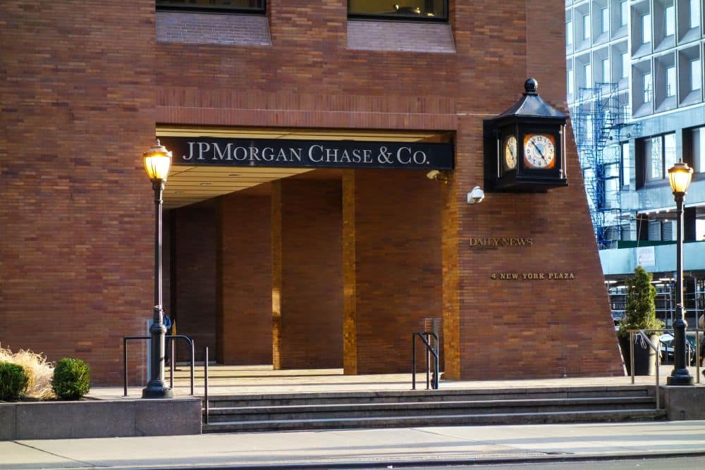 Eingang eines Gebäudes von JPMorgan Chase & Co. mit einem schwarzen Schild über dem Eingang, einer klassischen schwarzen Uhr an der Wand, einer Straßenlaterne und dem eingravierten Schriftzug "1 New York Plaza" in der Nähe des Eingangs - eine ikonische Szene im Financial District von New York.